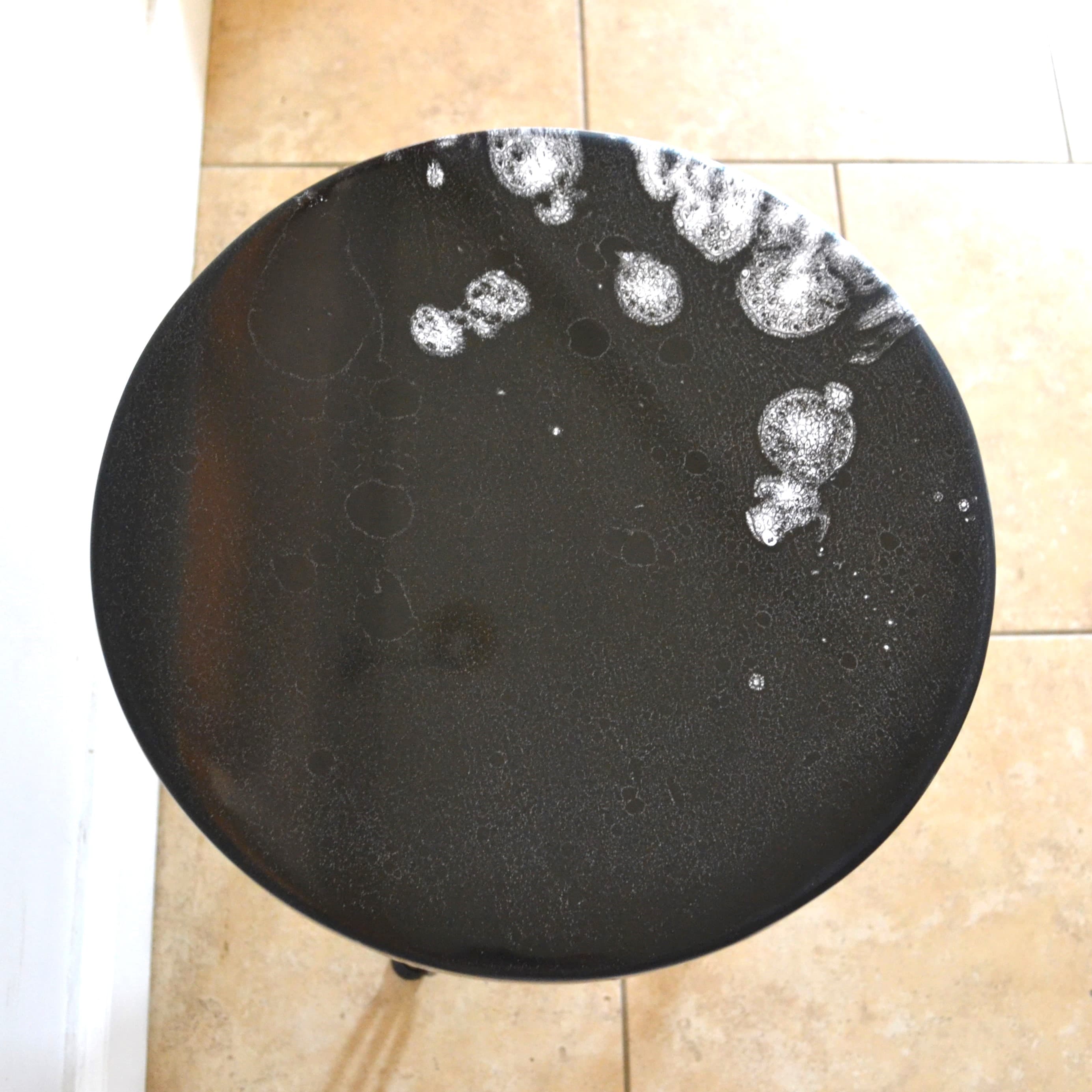 Overhead detail of a black round tabletop with white resin marks.