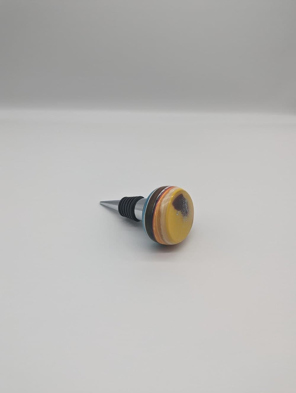 Upcycled wine stopper with layered resin top on a neutral surface.