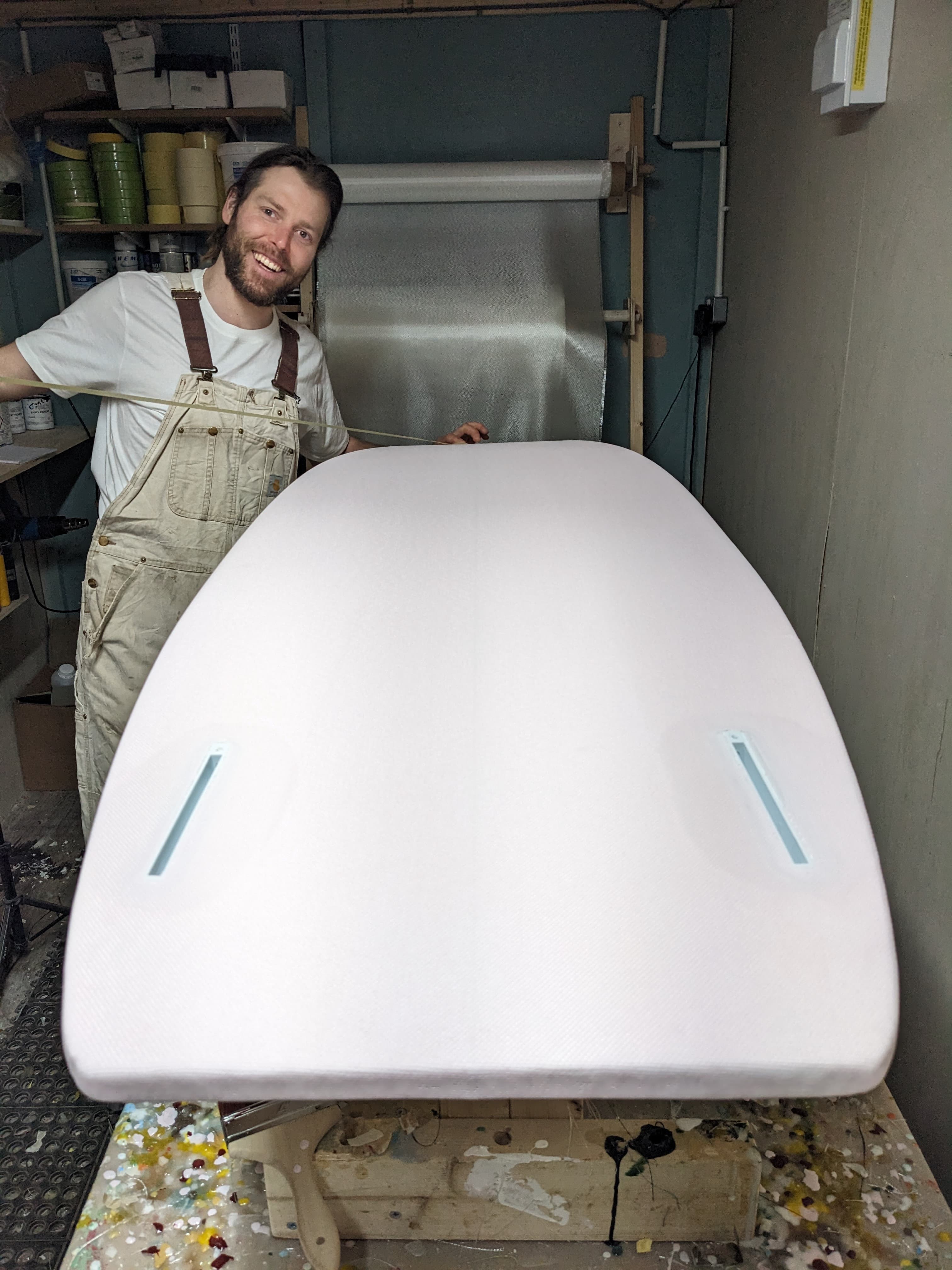 James standing in the workshop with a freshly shaped surfboard blank.