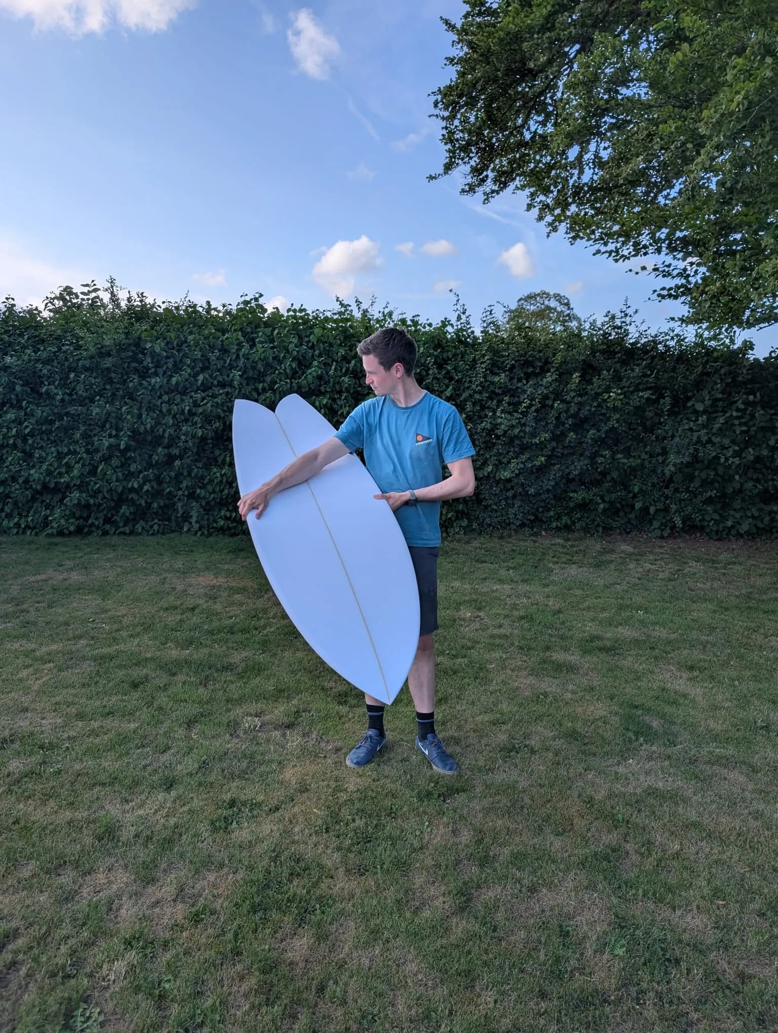 James holding a freshly shaped surfboard outside the workshop.
