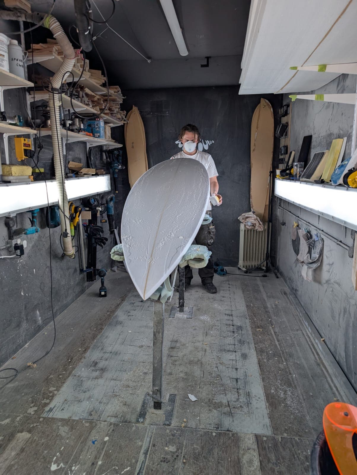 Close workshop view of a surfboard being shaped by hand.