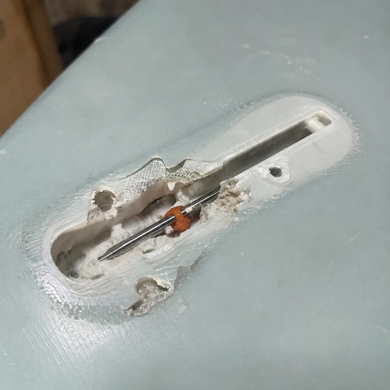 A damaged surfboard fin box with broken material around the fitting before repair.