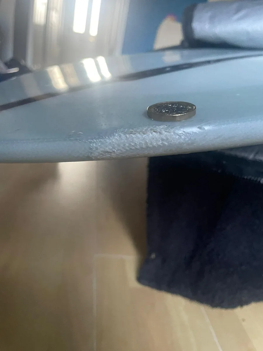 A cracked surfboard rail photographed beside a coin to show the extent of the damage.