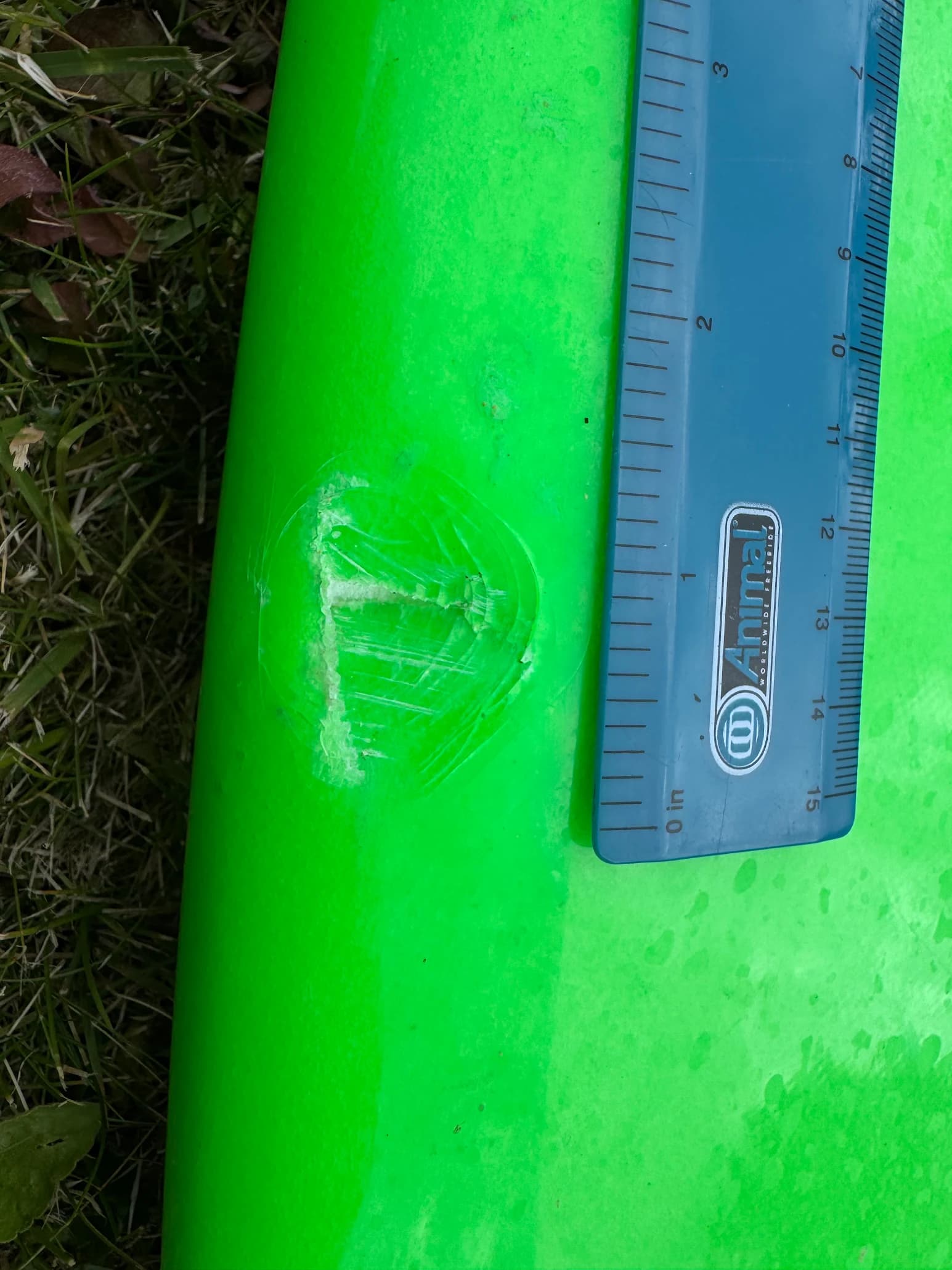 A small surfboard ding photographed beside a ruler to show the scale of the damage.
